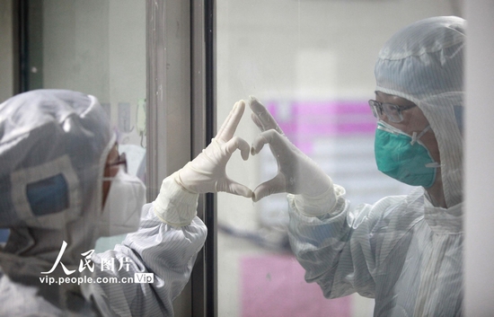 2月14日，在揚州市第三人民醫院新冠肺炎的隔離病房，一對醫生夫妻隔著玻璃做出愛心手勢。